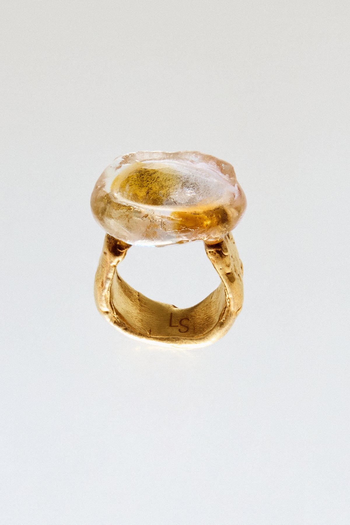 A gold ring with a large, organic-shaped translucent amber stone, photographed on a clean white background.