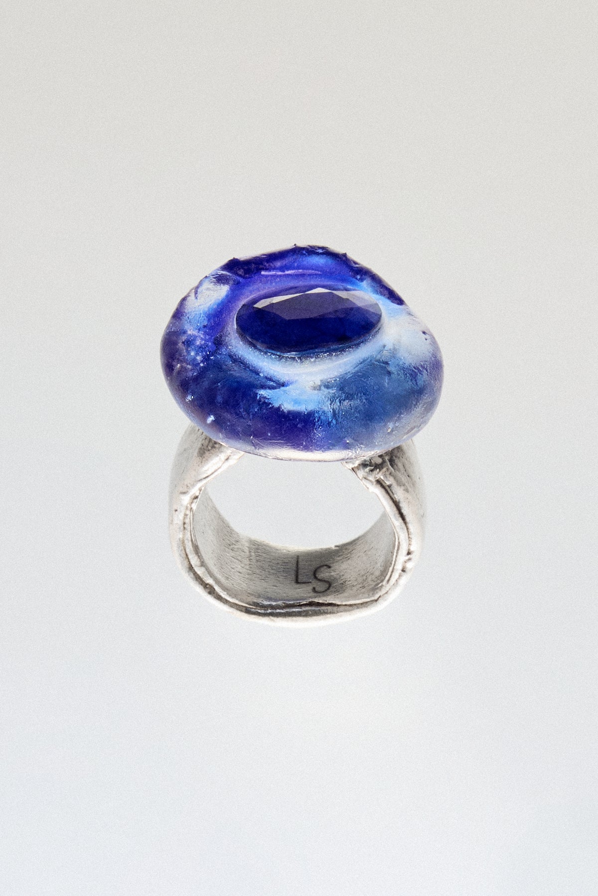 A handmade ring featuring a textured, organic-shaped cobalt blue glass dome on a rustic, hammered sterling silver band. The inside of the band is engraved with the initials 'LS'.