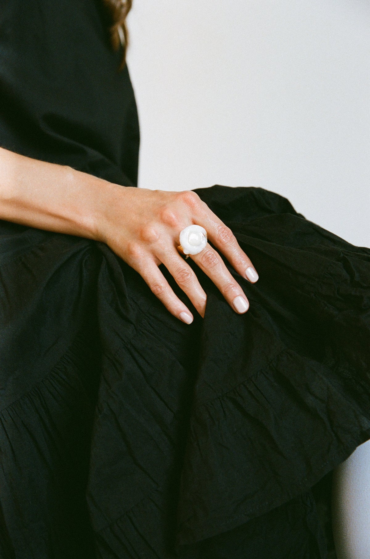 A close-up of a person's hand resting on a black dress, wearing a large white flower-shaped ring.