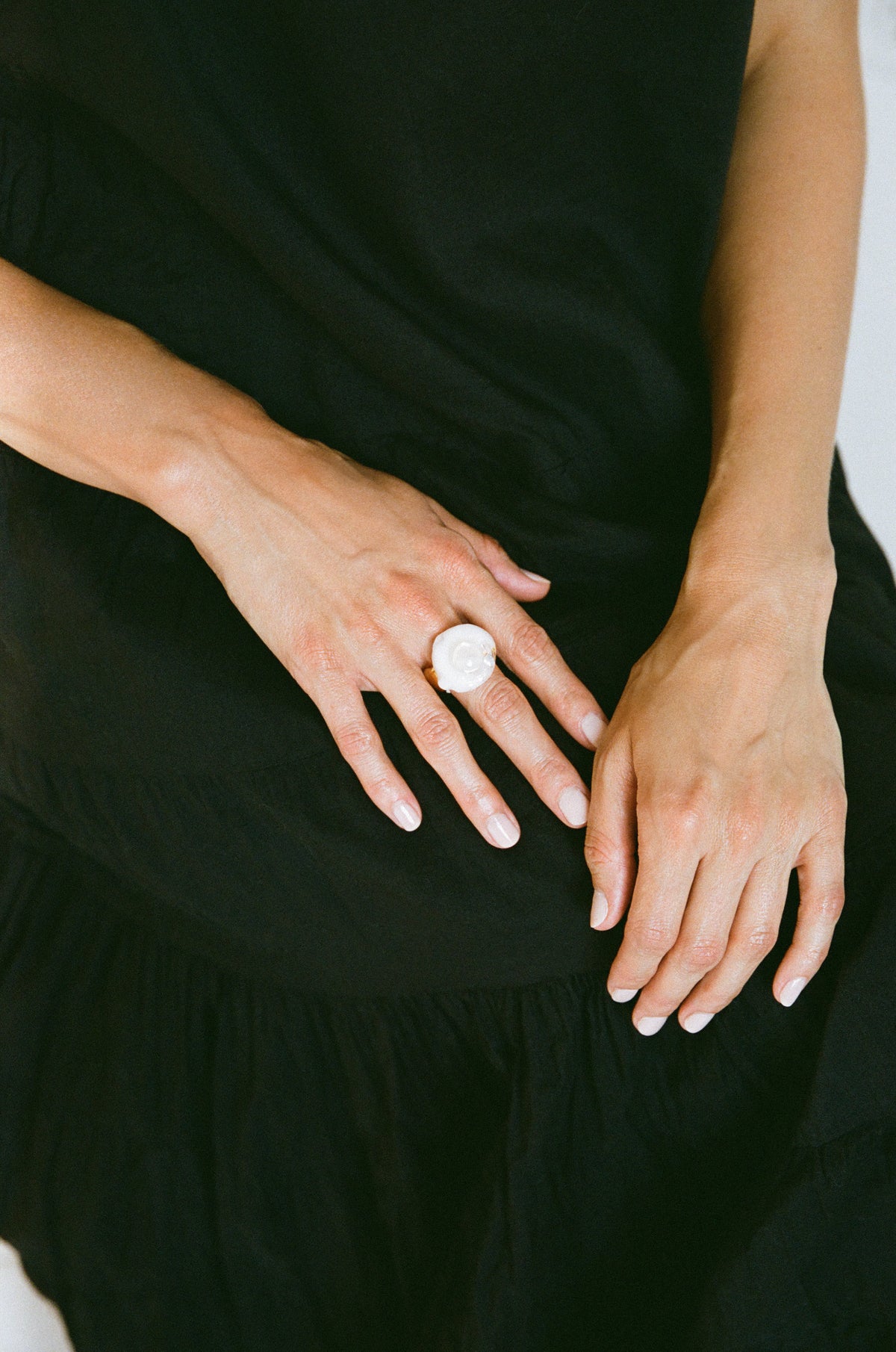 A close-up of a person's hands resting on their lap, wearing a large, round white ring with a silver-toned band.